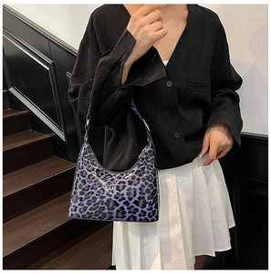 Close-up of purple leopard print glossy patent leather shoulder bag held by a model