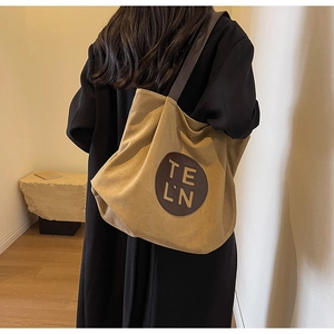 Close-up of khaki canvas tote bag featuring brown leather patch with TE LN lettering
