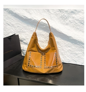 Detail of ginger yellow tote bag featuring silver hexagonal rivets and glossy leather texture