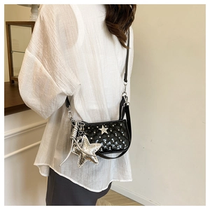 Detail of black quilted patent leather crossbody bag featuring a large silver star pendant