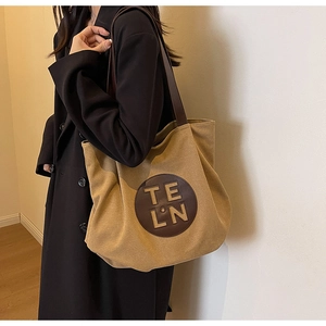 Close-up of khaki canvas tote bag with brown leather patch and shoulder strap on model