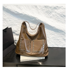 Detail of a brown glossy leather tote bag featuring stylish silver hexagonal metal rivets