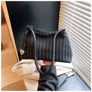 Detailed view of woven black tote bag featuring a vintage silver heart charm