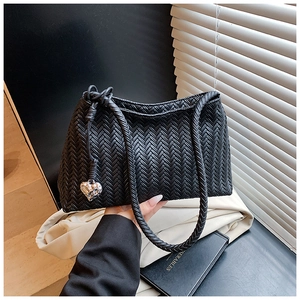 Close-up of black woven leather handbag texture with silver heart pendant detail