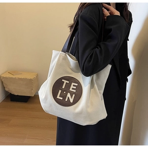 Detail of canvas tote bag with brown leather patch and shoulder strap on model
