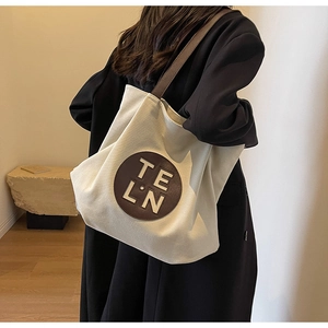 Detailed side view of a large cream canvas tote bag with dark brown shoulder straps