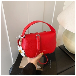 Detail view of red lychee grain leather handbag with floral pendant and metal buckle