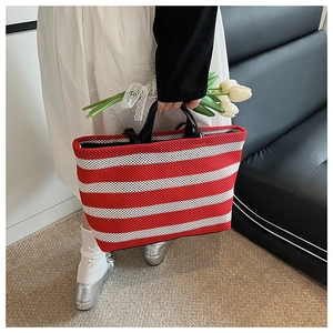 Détail du sac cabas en maille rayé rouge et blanc montrant la texture tissée et les anses noires