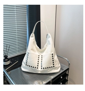 Close-up of a white punk hobo bag with silver hexagonal rivets on a metallic cart