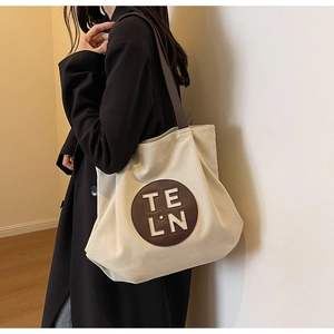 Detail of canvas tote bag showing the brown round logo patch and leather shoulder straps