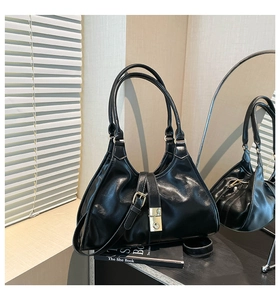 Sac sous le bras en cuir noir brillant avec boucle en métal doré posé sur un livre