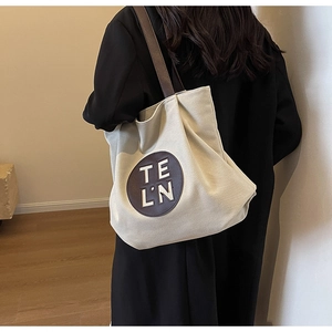 Detail of minimalist cream canvas tote bag with brown leather patch and shoulder straps
