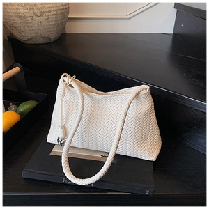 Detail of a creamy white woven bucket bag featuring a silver heart-shaped metal pendant