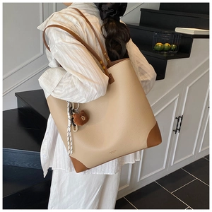 Rear view of a large beige tote bag with brown leather handles worn by a person on stairs