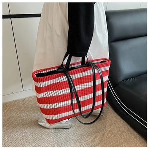 Détail du sac cabas en maille à rayures rouges et blanches avec anses noires sur canapé