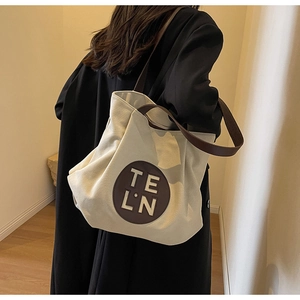 Detail of a large beige canvas tote with brown leather handles and stitched TE L.N patch
