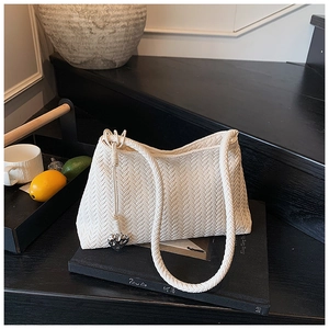 Close-up of cream woven shoulder bag featuring textured herringbone pattern and heart charm