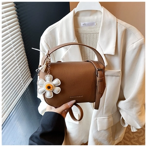 Detail of brown litchi pattern leather handbag with a white daisy floral charm