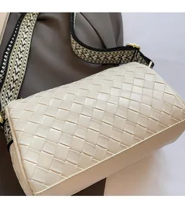 Close-up of beige woven pillow bag featuring wide wave-pattern fabric strap and gold hardware