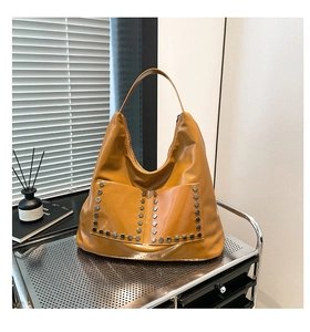 Detail of yellow hobo shoulder bag featuring glossy leather and metallic rivet accents
