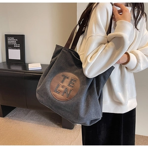 Dark grey canvas tote bag with brown leather patch and shoulder straps on a model
