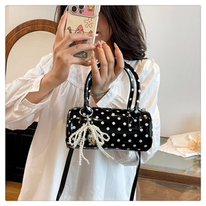 Détail du sac cylindre noir à pois avec un nœud en perles et un pendentif cœur