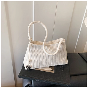 Macro detail of cream woven handbag with knot handle and heart charm on black leather