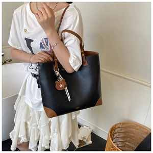 Detailed view of black lychee leather tote bag with brown trim and cute bear charm