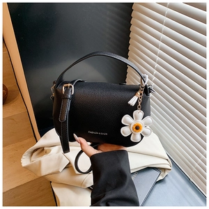 Close-up of black litchi pattern leather handbag with floral pendant and long shoulder strap