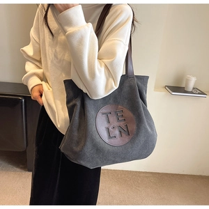 Detail view of large grey canvas tote bag with round leather patch and brown handle straps