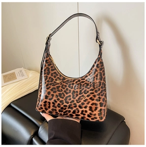 Detail of glossy leopard print crescent bag with golden hardware on artistic background