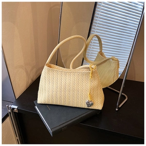 Detailed view of yellow woven shoulder bag with silver heart charm and textured pattern