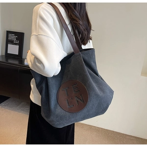 Detail of grey canvas tote bag with brown leather straps and letter patch on shoulder