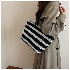 Détail d'un grand sac cabas tissé à rayures avec poignées en cuir porté par un mannequin