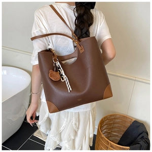 Detail of a brown lychee pattern leather tote bag with a cute plush bear charm on the strap