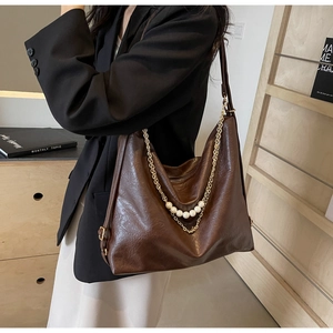 Detail of dark brown tote bag featuring elegant pearl and gold chain strap decorations