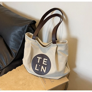 Detail of off-white canvas tote bag featuring brown leather straps and a circular logo patch