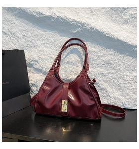 Détail du sac sous le bras en cuir verni bordeaux avec fermoir doré et soufflets latéraux