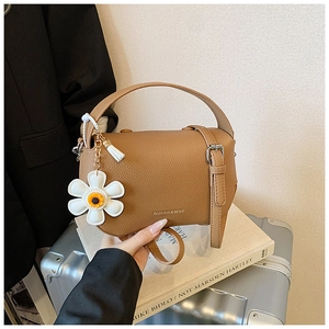 Detail of tan lychee pattern handbag with a white daisy charm and removable strap