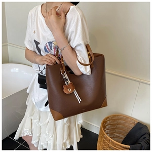 Detail of dark brown faux leather tote with cartoon bear charm and contrast corners
