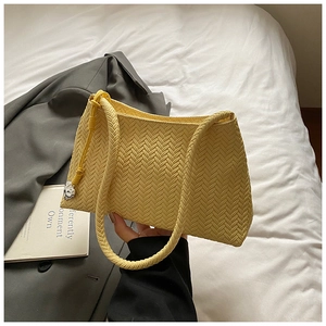 Detail of yellow woven faux leather shoulder bag with silver heart charm and braided handle