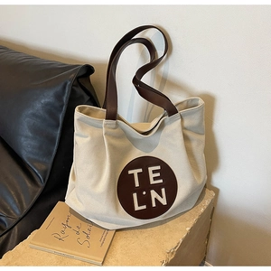 Detail of beige canvas tote bag with brown leather handles and circular logo patch
