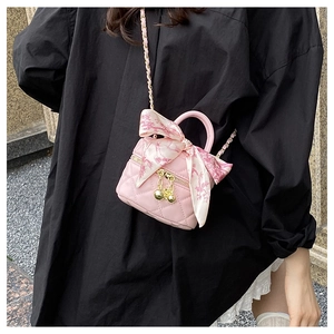 Detail of pink quilted mini bag with gold ball pendants and silk scarf on a model