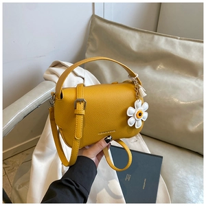 Detail of a ginger yellow lychee leather handbag with a daisy charm and silver buckle