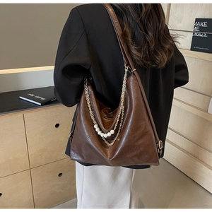 Detail of a brown oil-wax leather tote bag with pearl and gold chain on model's shoulder