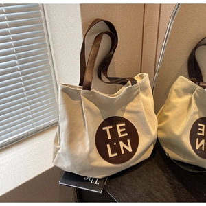 Detailed view of canvas tote bag showing the leather logo patch and sturdy top handles