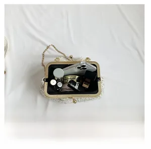 Detailopname van het ruime interieur van de witte geweven clutch met gouden kettingriem