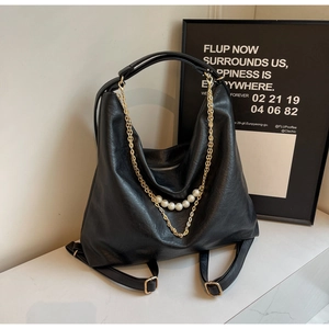 Close-up of black leather tote bag featuring gold chain and white pearl decorations