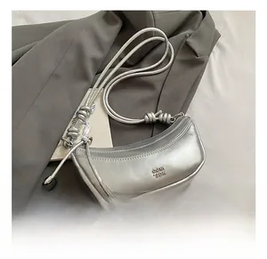 Détail du sac demi-lune argenté avec bandoulière à nœuds posé sur une veste grise