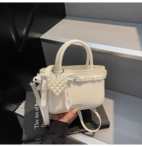 Detailansicht der cremefarbenen Kunstledertasche mit Perlenherz und Spitzen-Schleife